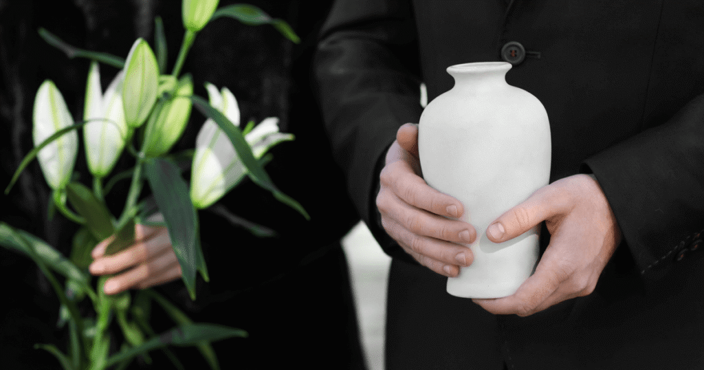 Person in a black suit holding a plain white ceramic cremation urn