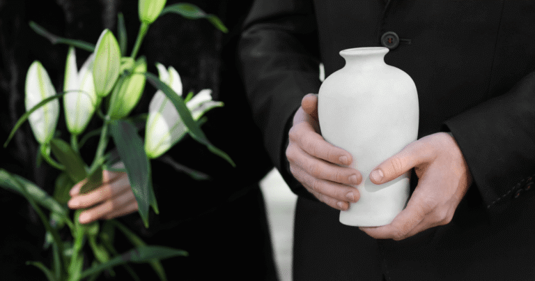 Person in a black suit holding a plain white ceramic cremation urn